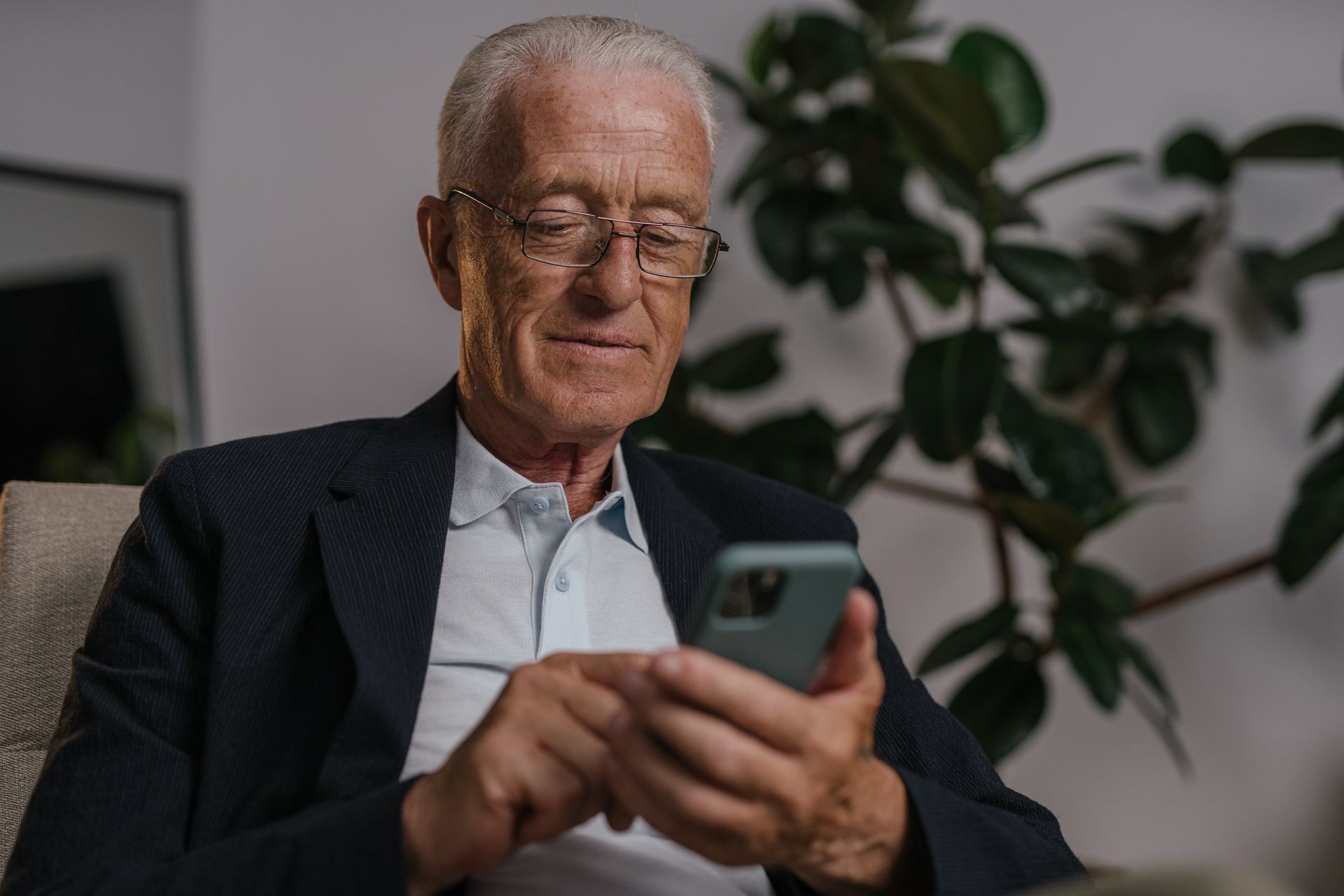 An Elderly Man in Black Suit Wearing Eyeglasses while Using His Mobile Phone