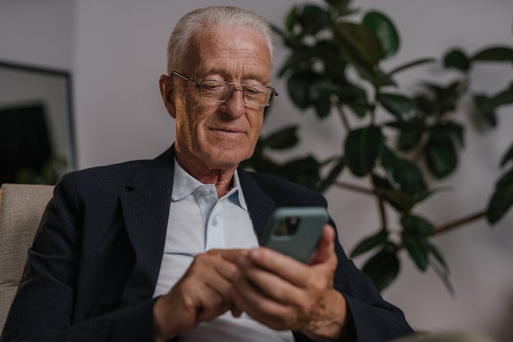 An Elderly Man In Black Suit Wearing Eyeglasses While Using His Mobile Phone