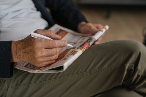 Free Close-up of a senior adult solving a crossword puzzle in a newspaper with a pen. Stock Photo