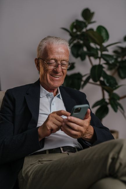 Elderly man smiling while using a smartphone indoors