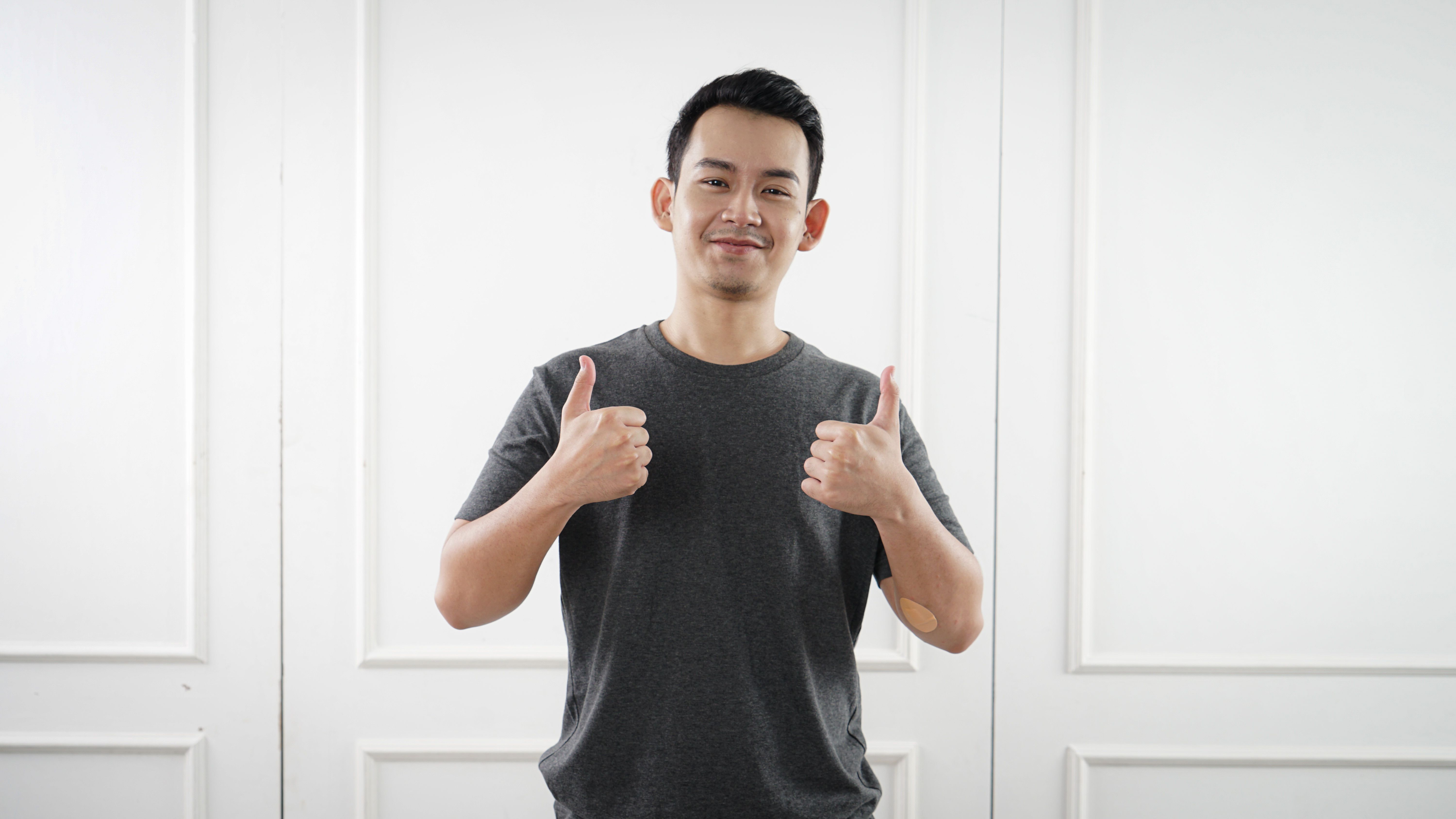 Asian man in a grey t-shirt showing thumbs up with a smile indoors in Jakarta.