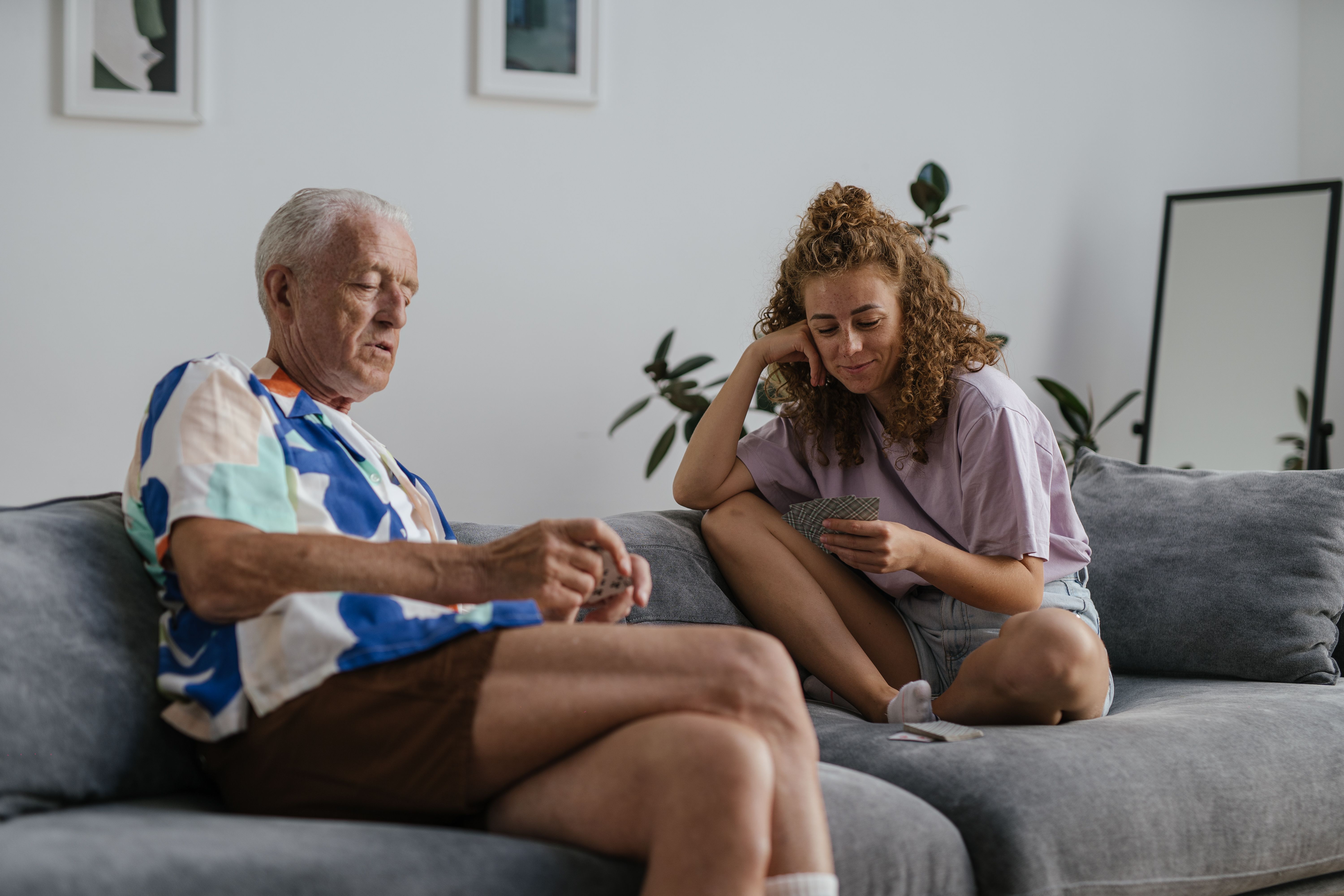 Elderly man and young woman enjoy a card game on the sofa, fostering bonding and leisure.