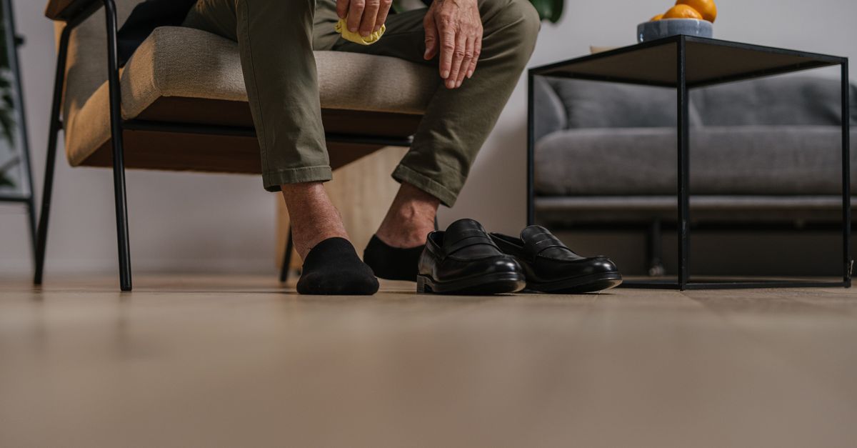 Man sitting on chair with black leather shoes on floor. Minimalist interior with plants.