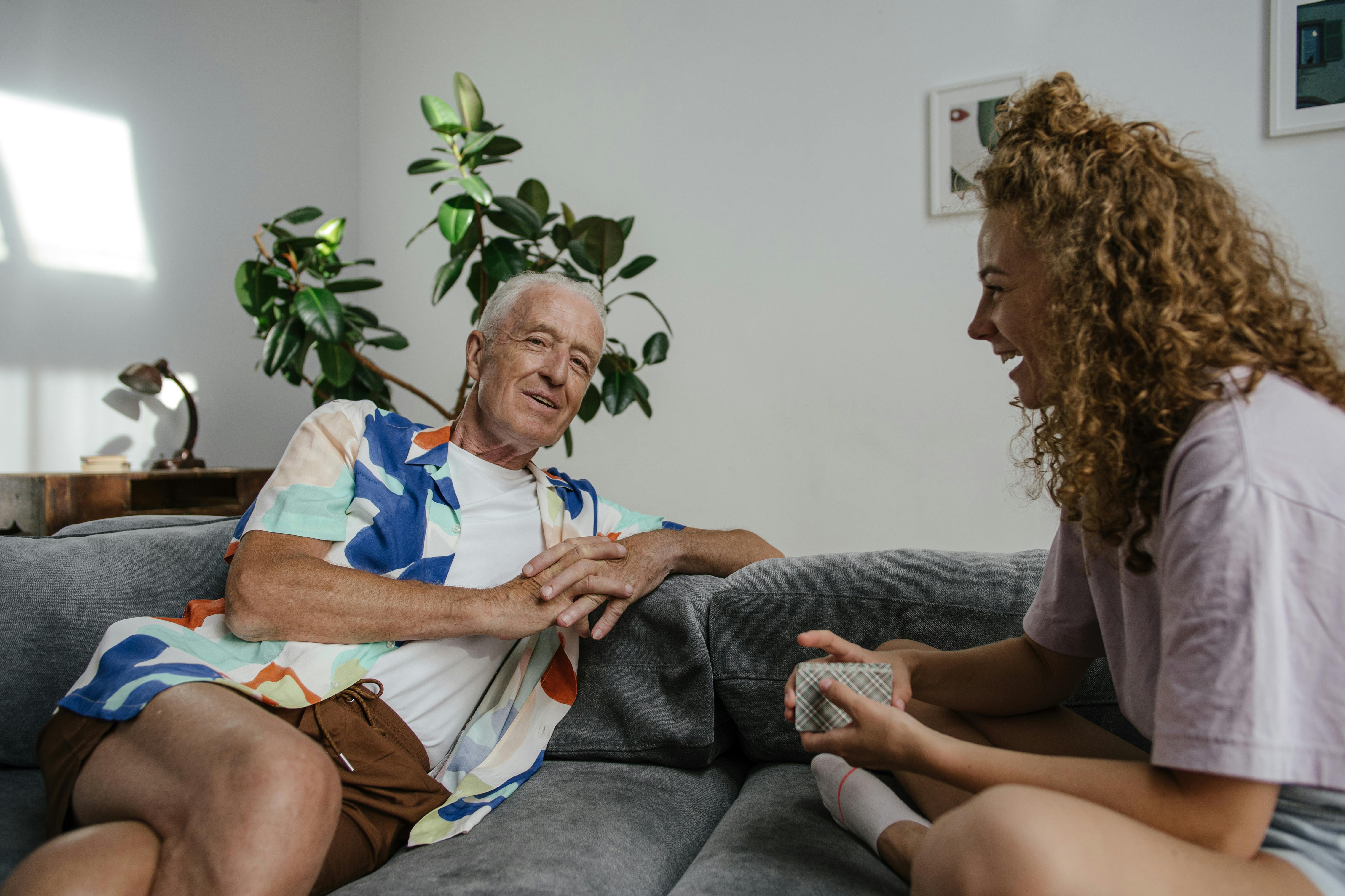 an elderly man talking to his granddaughter while sitting on the couch