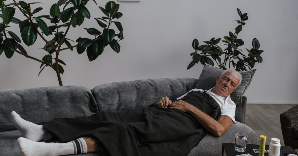Elderly man resting on a sofa near a side table with pill bottles and a glass of water