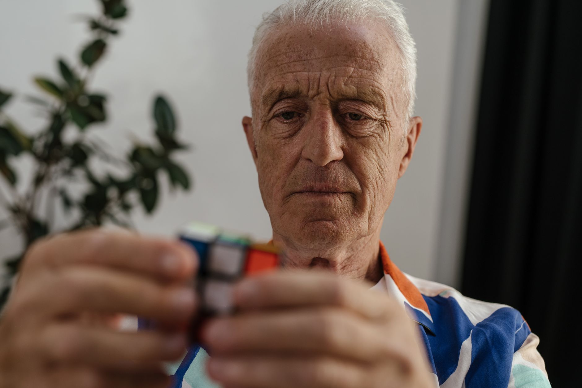 Elderly man concentrating on solving a Rubik's Cube, showcasing focus and mental agility.