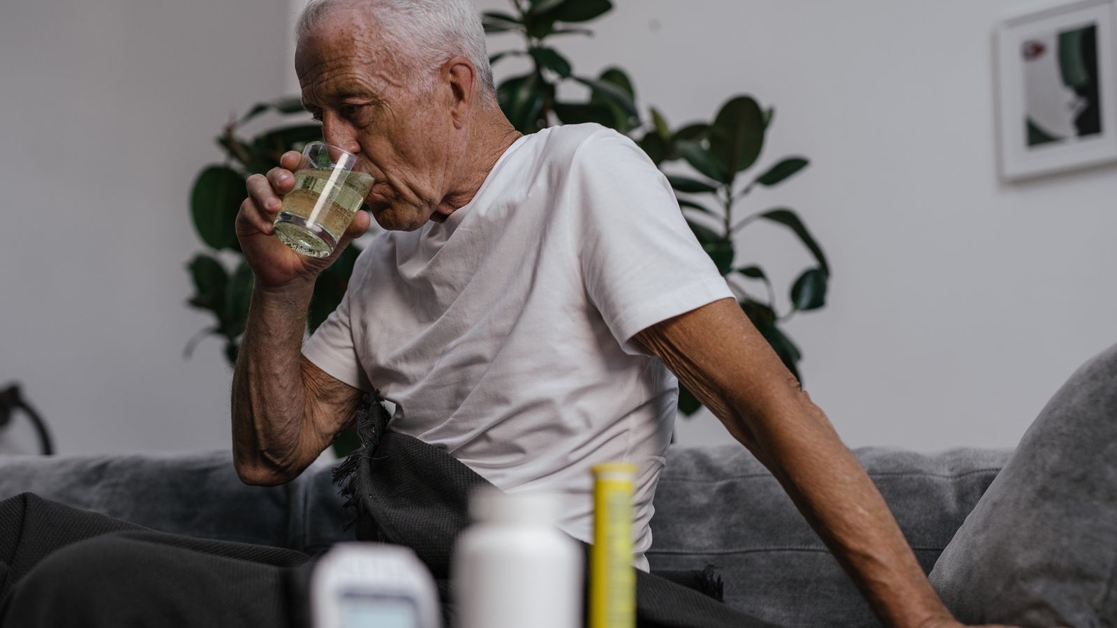 Senior man in white shirt drinking medicine indoors. Health and wellness lifestyle.