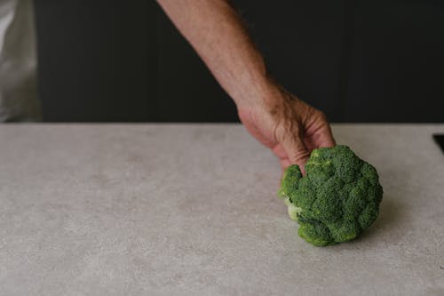 Free Person Holding a Broccoli on Table   Stock Photo