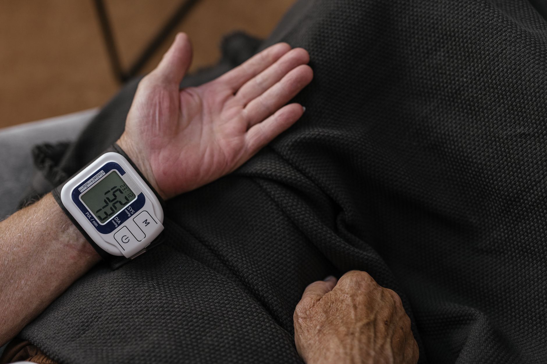 A senior adult using a wrist blood pressure monitor at home, focusing on health management.