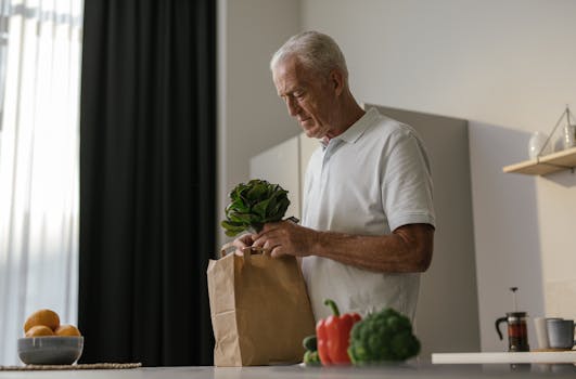 Senior man in a white polo shirt unpacking vegetables in a modern kitchen setting.