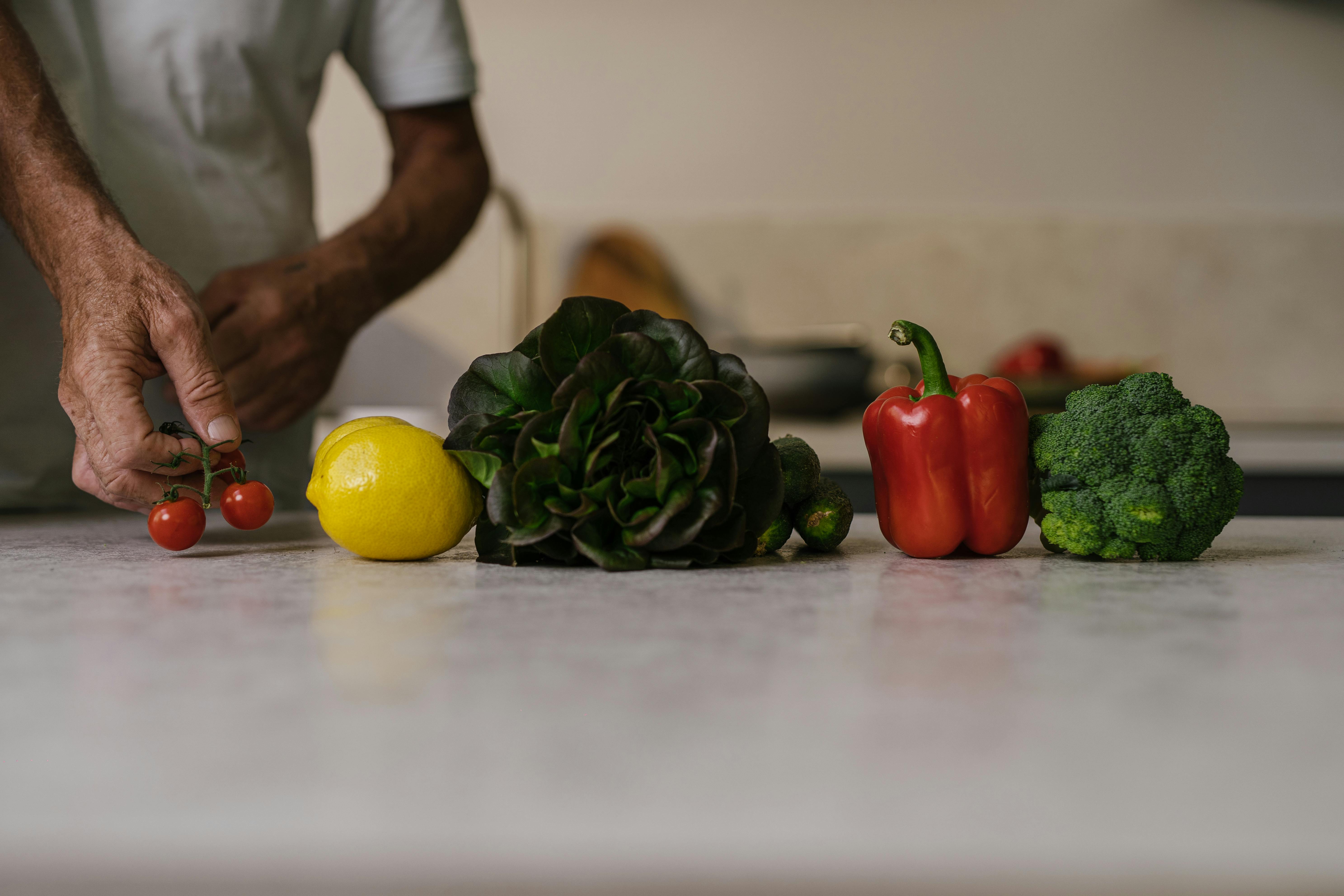 Close-up of fresh vegetables and fruit on a kitchen counter with a person arranging them.