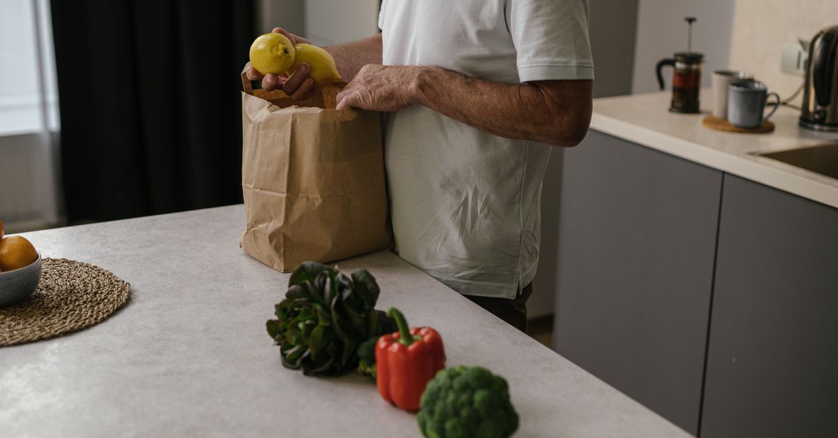 Uma pessoa organiza frutas e verduras frescas em um ambiente de cozinha moderna.
