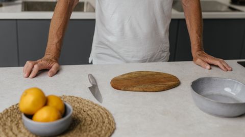 Adult man standing in a modern kitchen preparing to slice lemons with a knife.