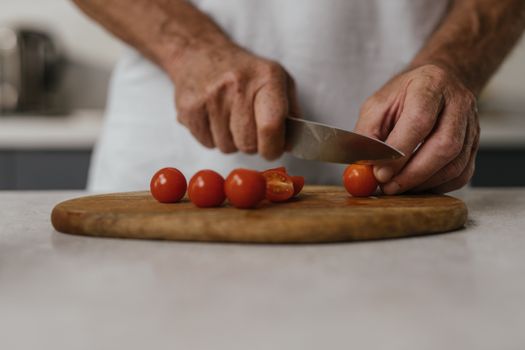 Hands slicing fresh cherry tomatoes on a wooden board in a kitchen setting.