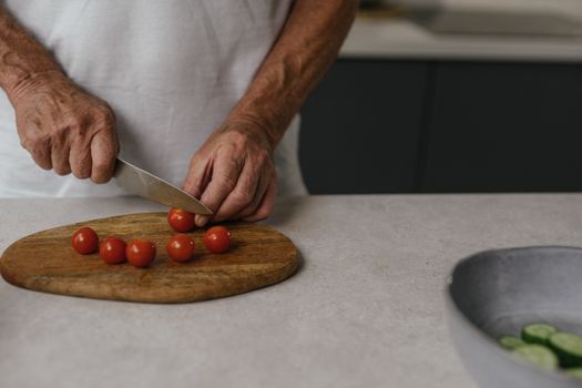 Close-up of a man slicing cherry tomatoes on a wooden cutting board in a kitchen setting.