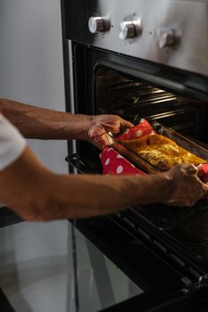 Adult putting a baking dish in the oven using a red polka dot cloth, showcasing home cooking.