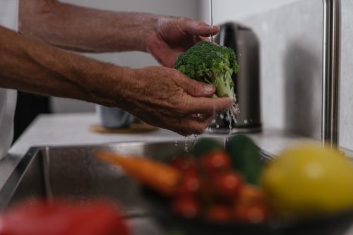 Free Hands washing broccoli under running water in a kitchen sink, healthy cooking concept. Stock Photo