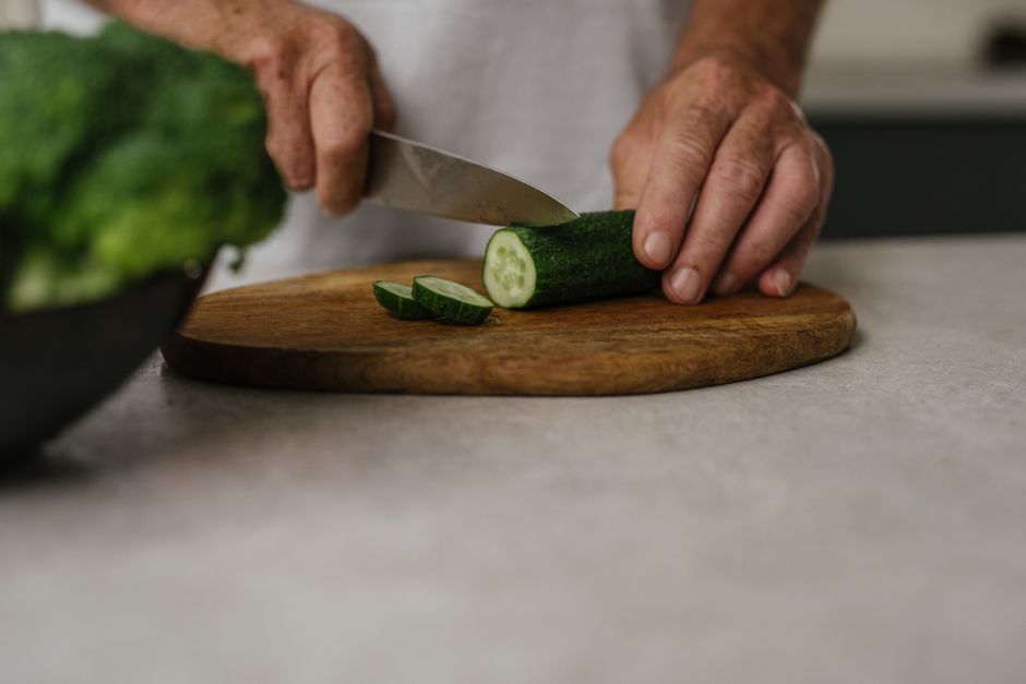 Close-up of hands slicing cucumber on wooden board in kitchen setting.