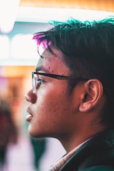 Side profile of a young man wearing glasses, illuminated by neon lights, creating a vibrant urban feel.