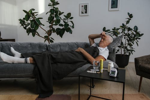 Free A Sick Man May in White Shirt Lying Down on Gray Sofa Stock Photo