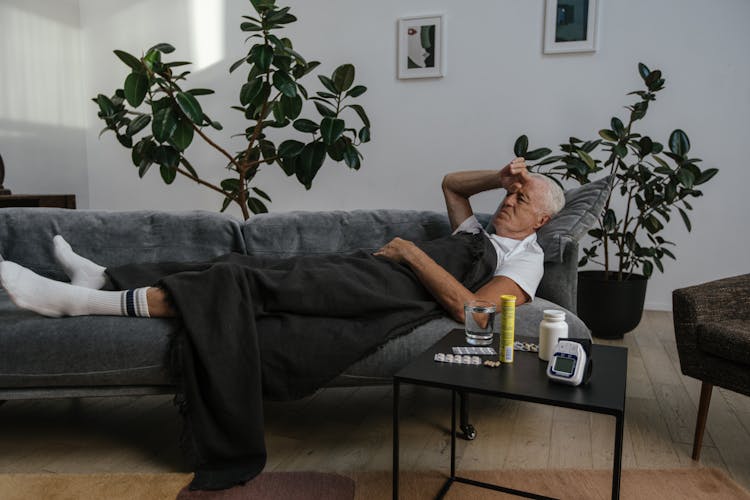 A Sick Man May In White Shirt Lying Down On Gray Sofa