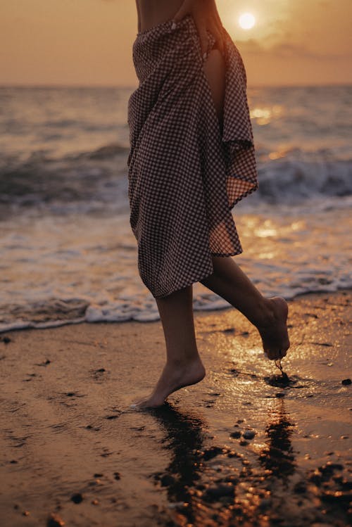 A Woman in Printed Skirt Walking on the Beach Barefooted