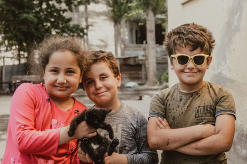Free Three smiling children playing with a black kitten in a sunny outdoor setting. Stock Photo