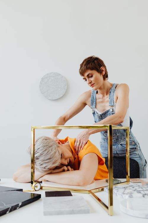 Free Two women indoors, one giving a shoulder massage to the other in a casual setting. Stock Photo
