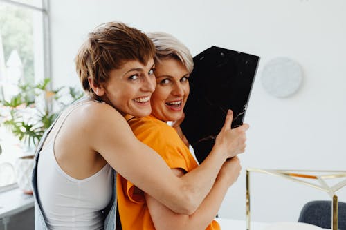 Woman in White Spaghetti Strap Top Hugging a Woman in Orange Shirt