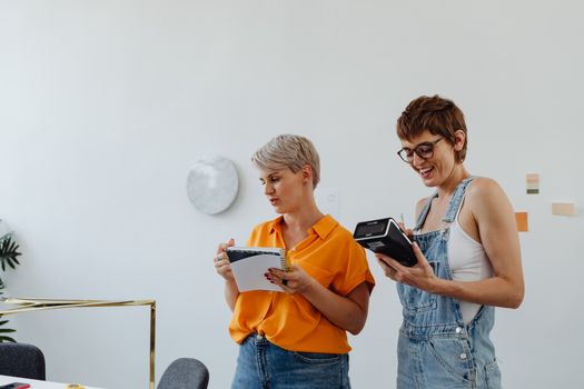 Two women collaborating in a modern workspace, discussing ideas with a notebook and a device.