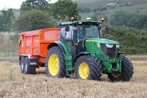 Free A green tractor pulling an orange trailer in a wheat field in Warminster, England. Stock Photo