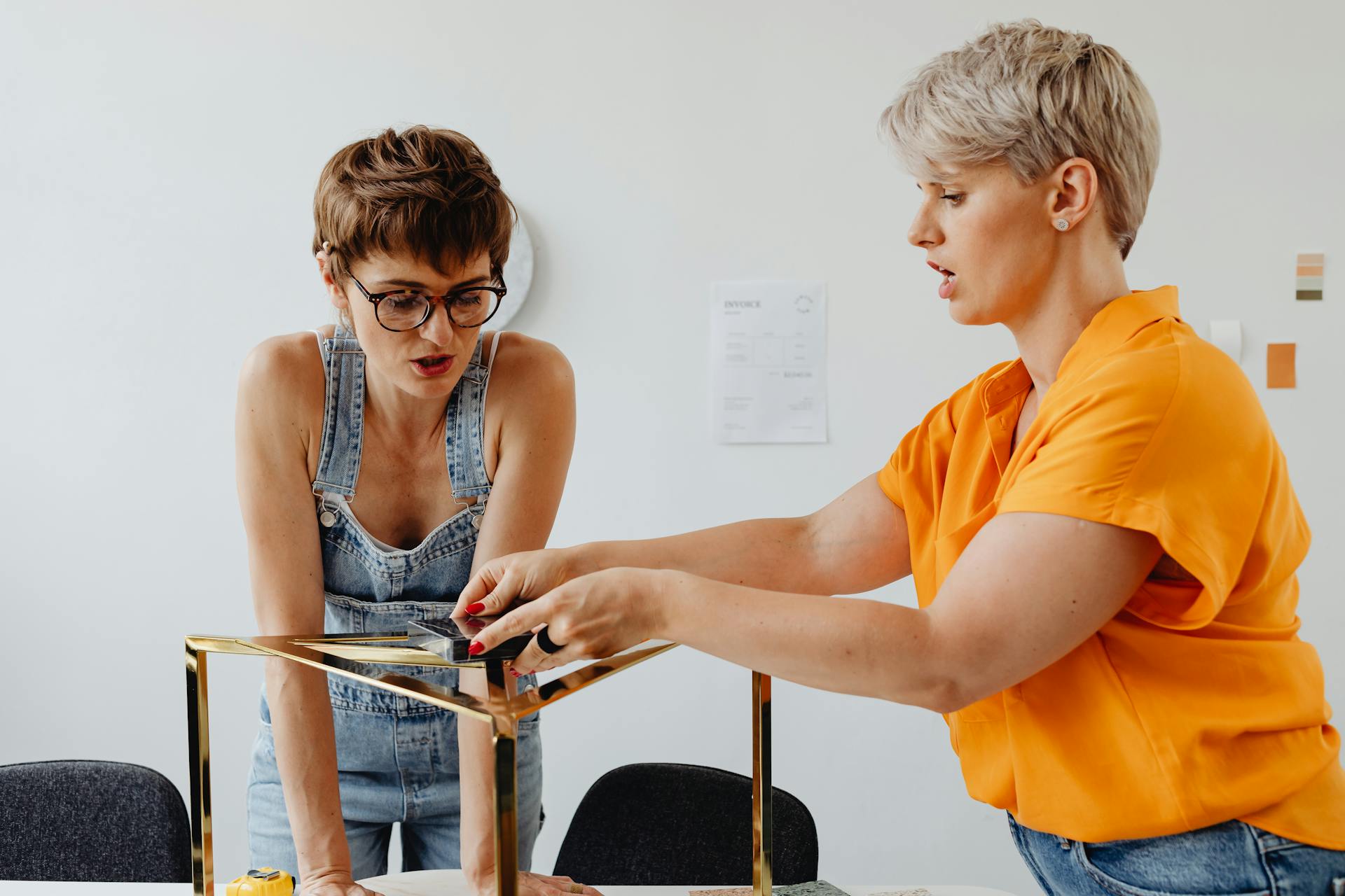 Two women collaborating on a furniture design project in a workshop setting.