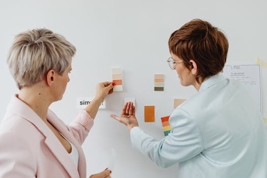 Two women collaborating on design elements, with paint swatches on a wall.