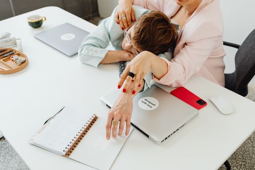 Free Two women in business attire relaxing together at a desk, surrounded by laptops and a notebook. Stock Photo