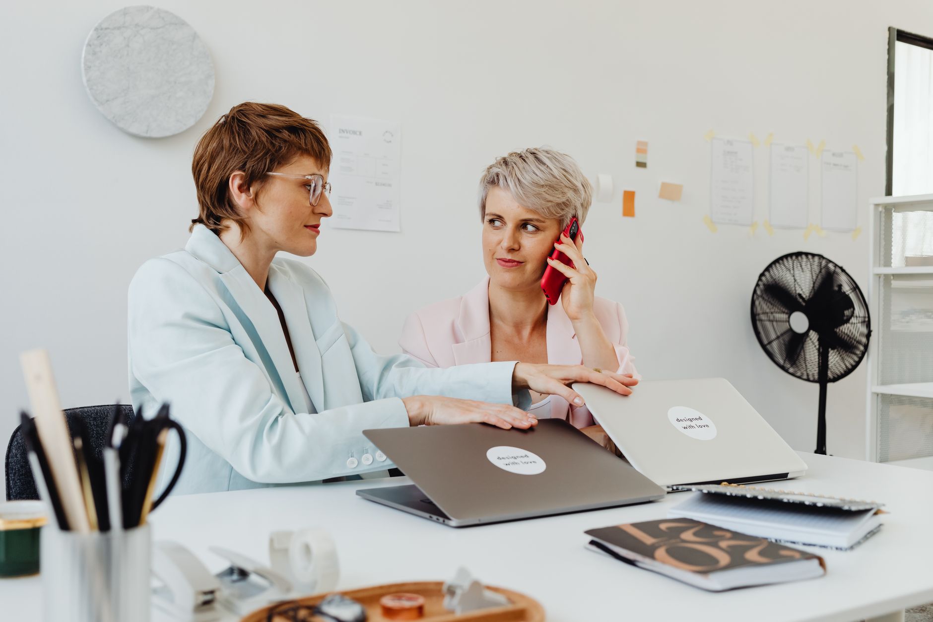 Two businesswomen collaborating at a desk with laptops in a modern office environment.