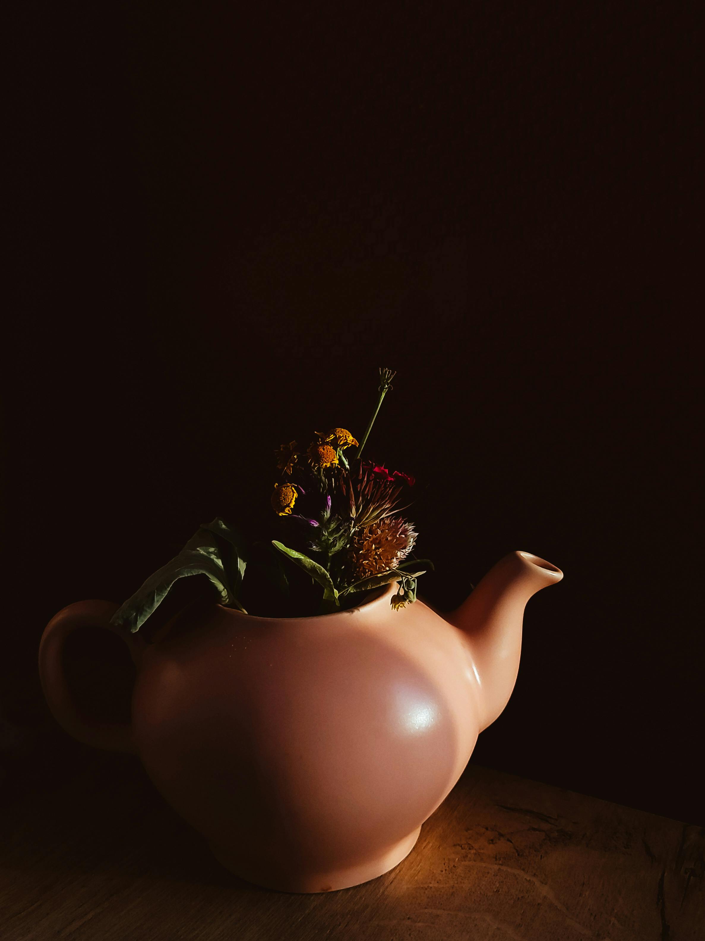 A creative ceramic teapot adorned with vibrant flowers against a dark backdrop.
