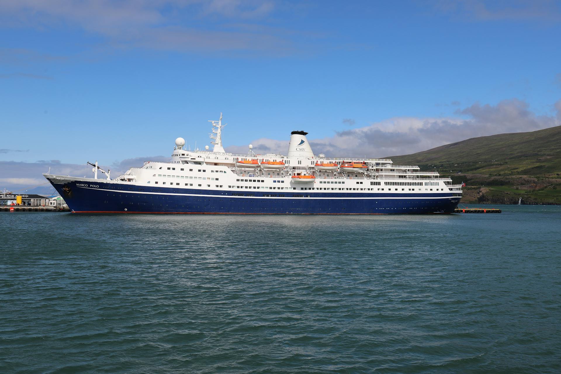 A cruise ship sails through calm Icelandic waters under a blue sky, showcasing leisure travel.