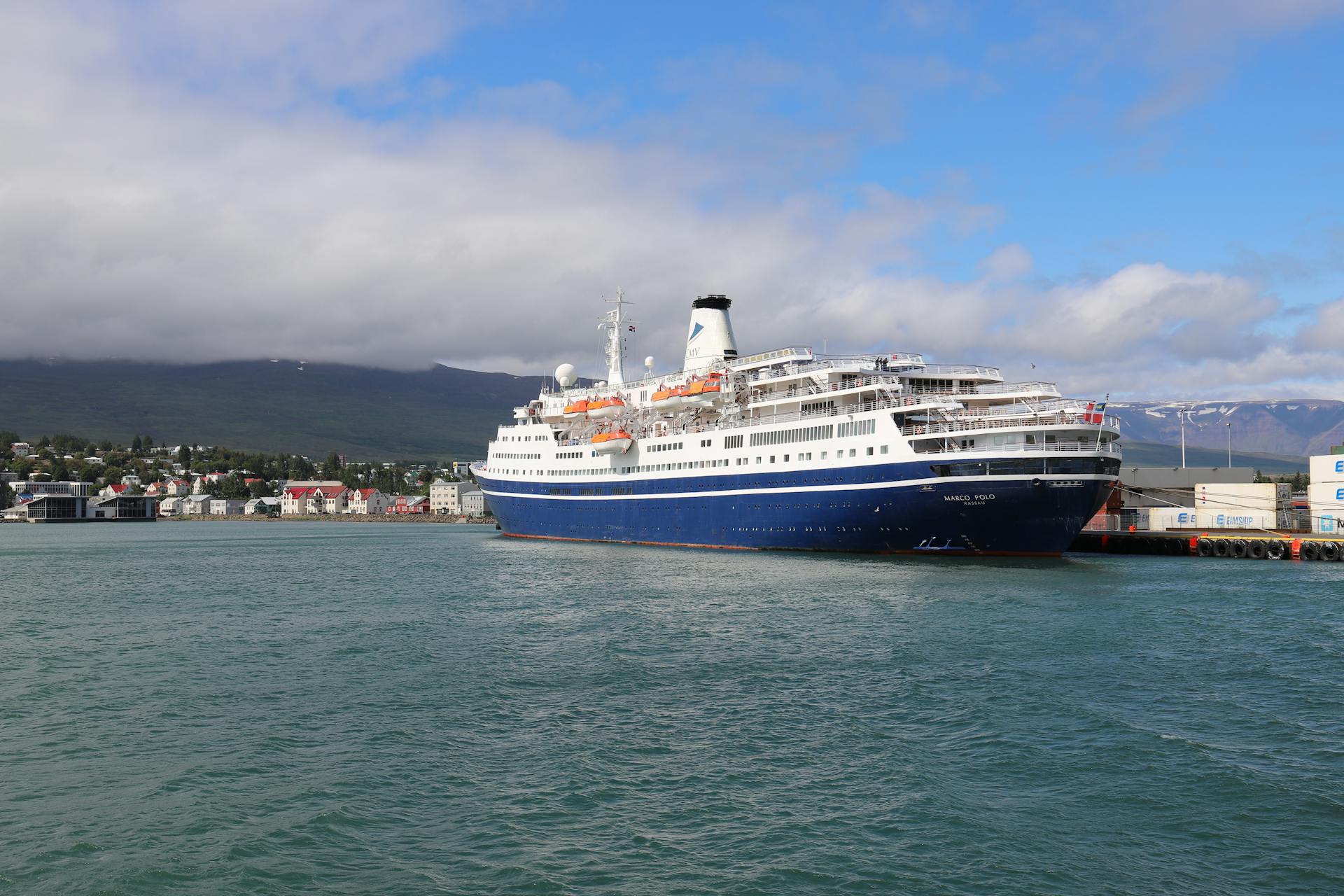 Scenic view of a cruise ship docked at Akureyri harbor with a mountainous backdrop in Iceland.