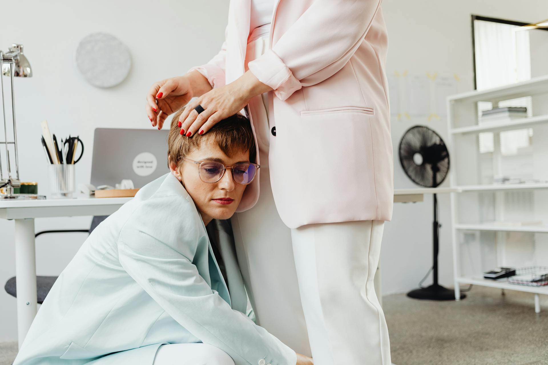 Two women embracing, offering emotional support in a contemporary office environment.