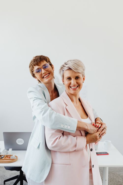 Free Two smiling businesswomen in blazers embracing affectionately in a bright office. Stock Photo