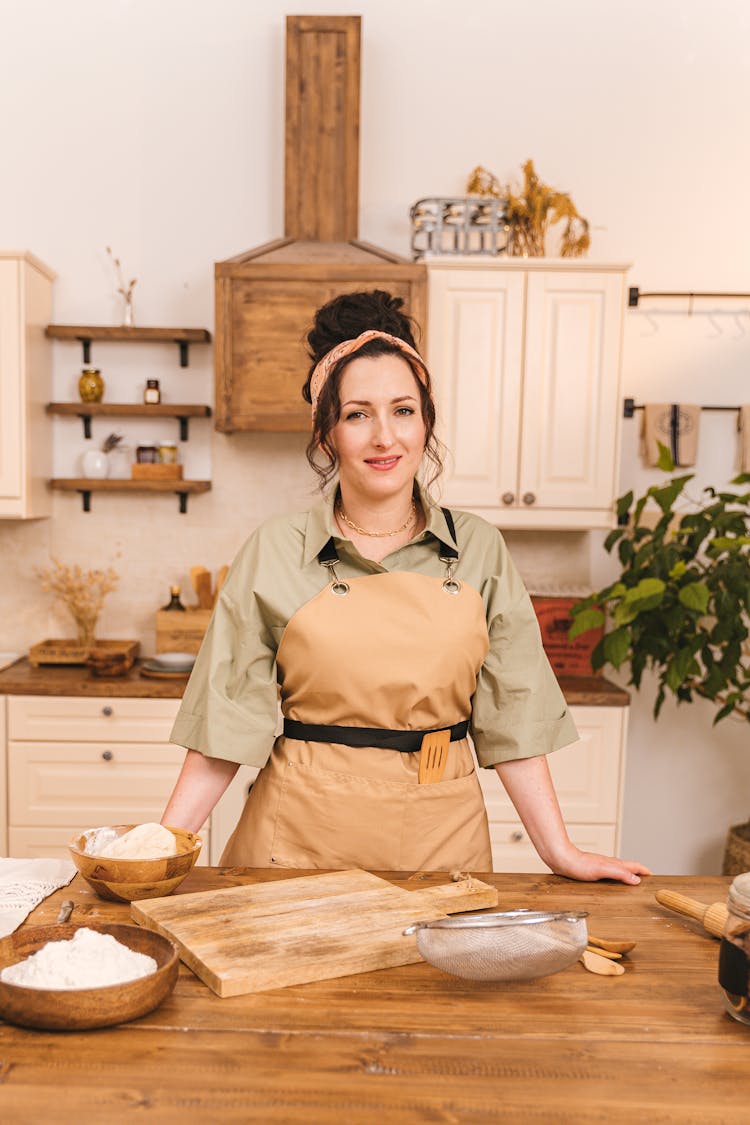 Woman In Brown Apron Standing Behind A Wooden Kitchen Counter 