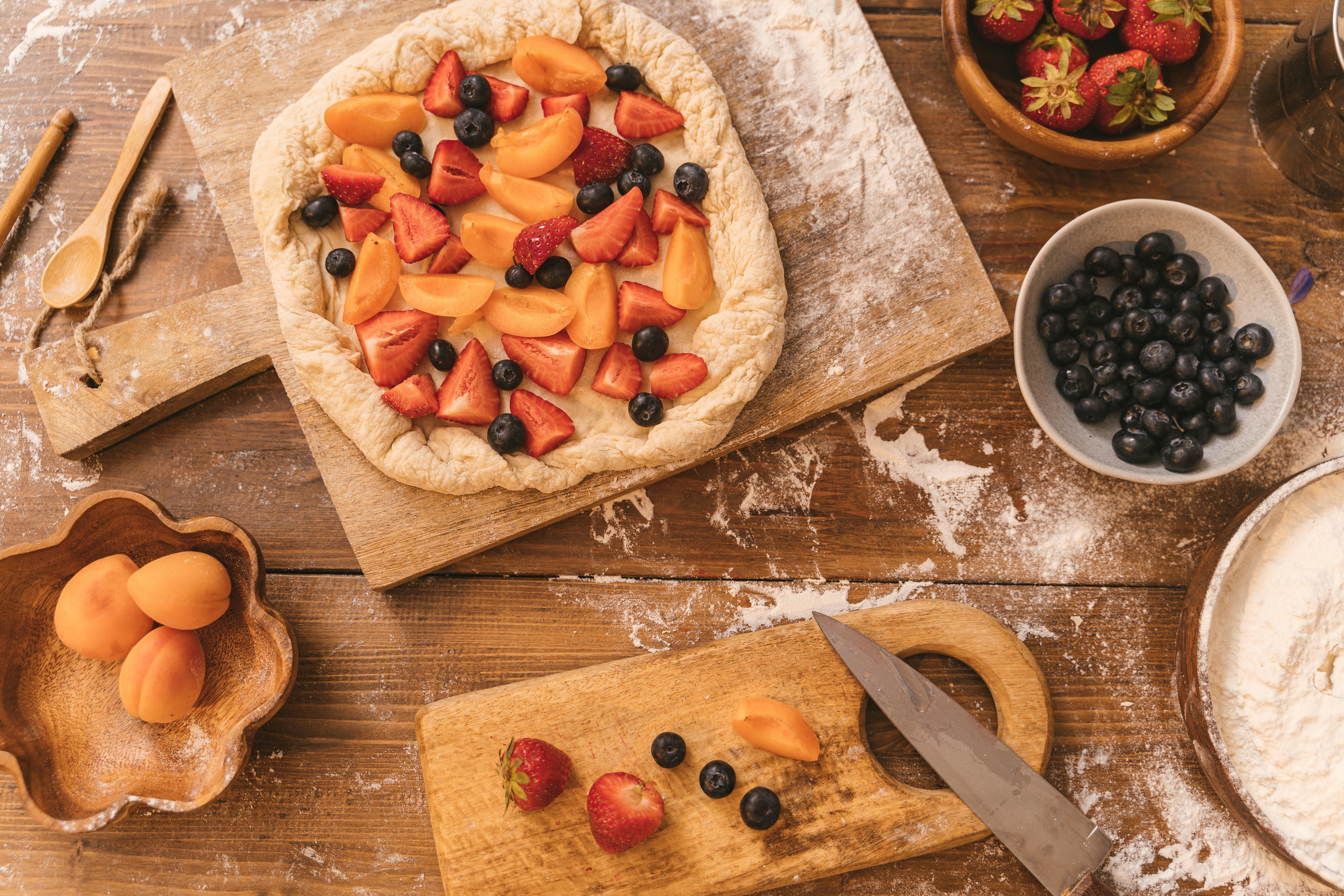 A fresh fruit tart with blueberries and strawberries on a wooden cutting board.