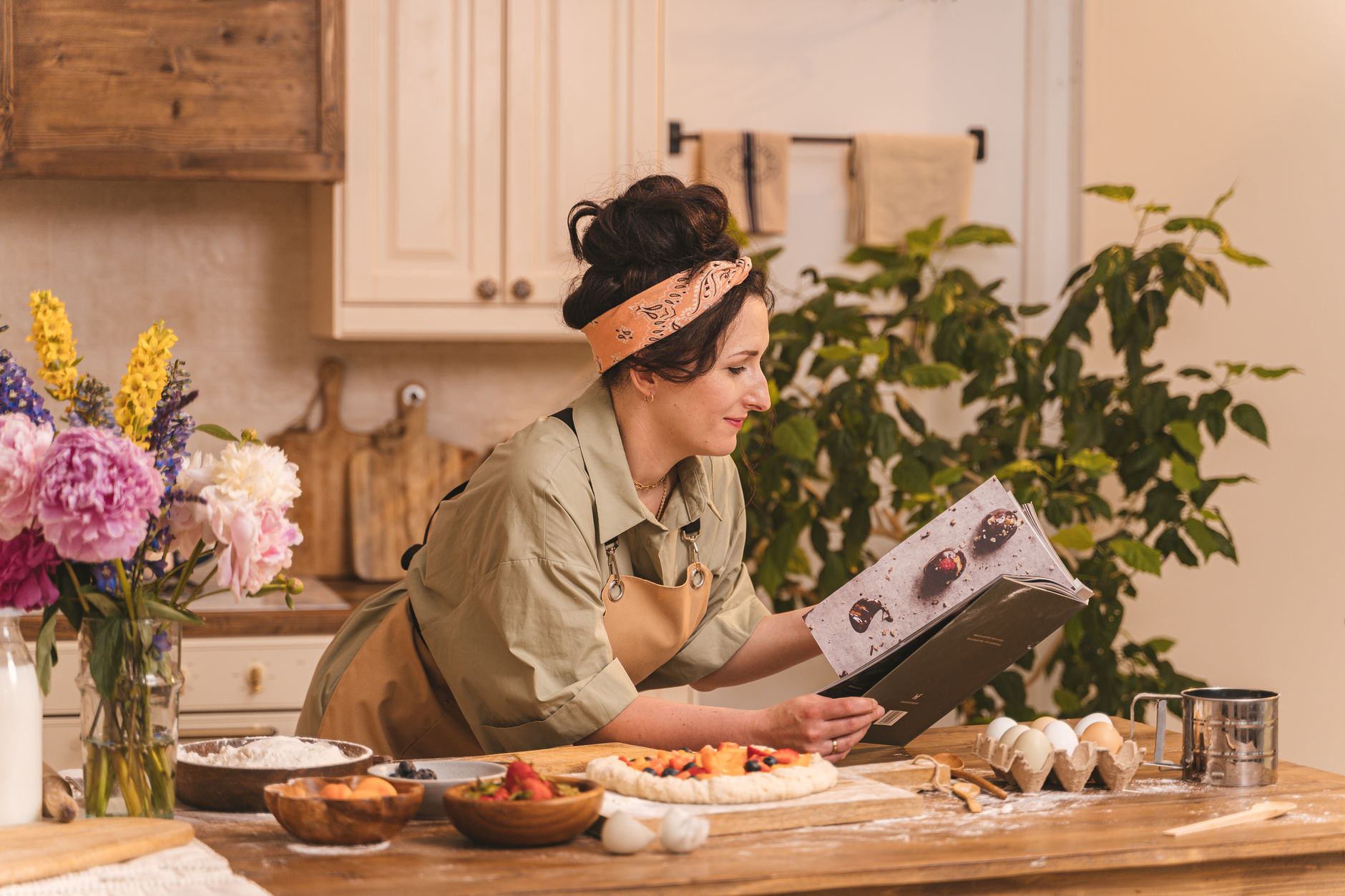woman cook at a wooden kitchen table with cookbooks and produce