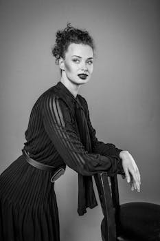 Black and white portrait of a woman leaning on a chair, showcasing elegance and style.