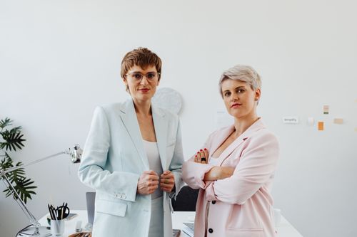 Free Two confident businesswomen in stylish suits pose together in a bright and modern office setting. Stock Photo