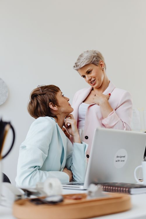 Free Two women in colorful suits share a moment at the office with a laptop. Stock Photo