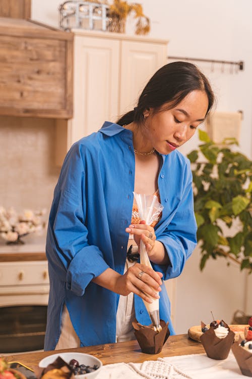 Woman in Blue Dress Shirt Decorating A Cupcake With Icing