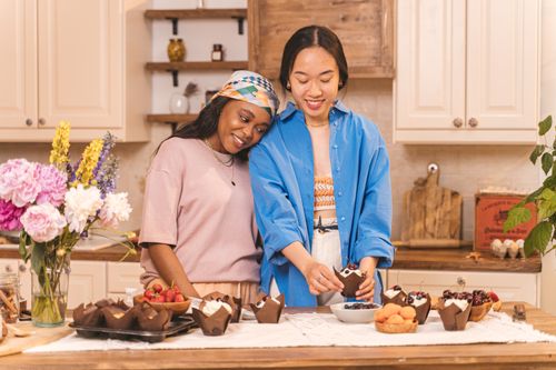 Free Two friends enjoy baking cupcakes together in a warm, inviting kitchen setting. Stock Photo