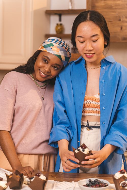 Free Two friends smiling and enjoying homemade pastries in a cozy kitchen setting. Stock Photo