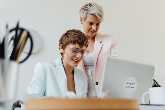Two professional women working together happily on a laptop in a bright office setting.